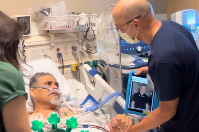 Paul Aguilar is in his hospital bed, with nurse David Yamada standing by his side, grasping his hand. Yamada is also holding a tablet with the message from Sylvester Stallone.