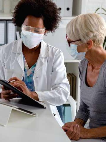 A doctor with a face shield 和 mask discussing with a masked patient.